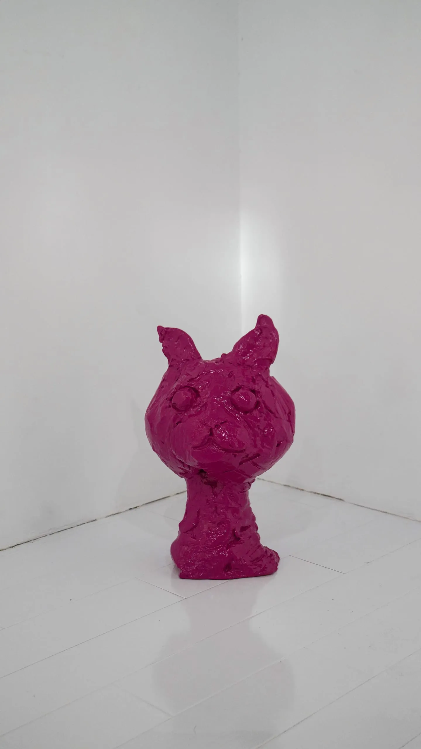 A roughly modelled magenta cat bust standing in the corner of the white gallery.